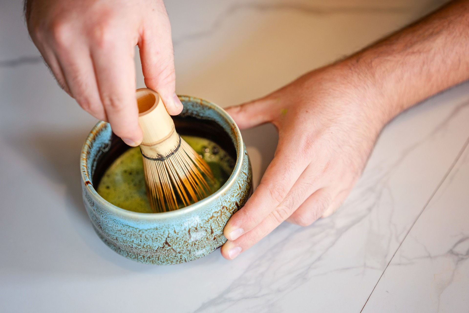 Hands of barista mixing green Matcha tea with bamboo whisk
